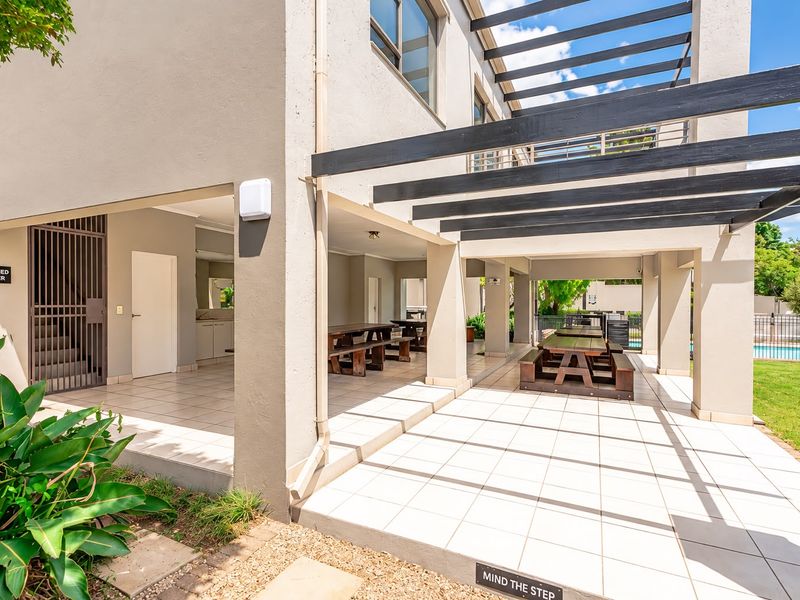 A spacious covered patio area featuring tiled flooring, a pergola structure, and direct access to the garden and pool area.