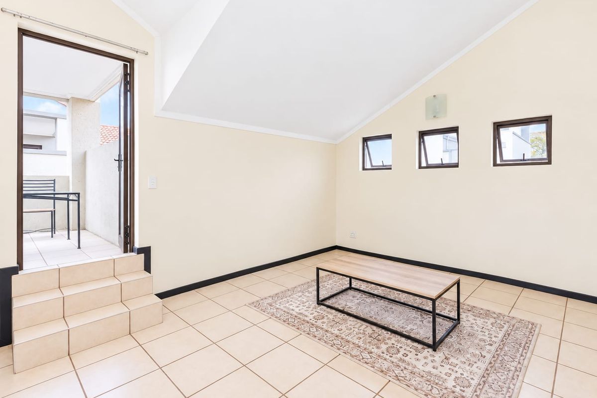 A bright, open-plan living area featuring vaulted ceilings, tiled flooring, and direct access to an outdoor patio via a small set of tiled steps.