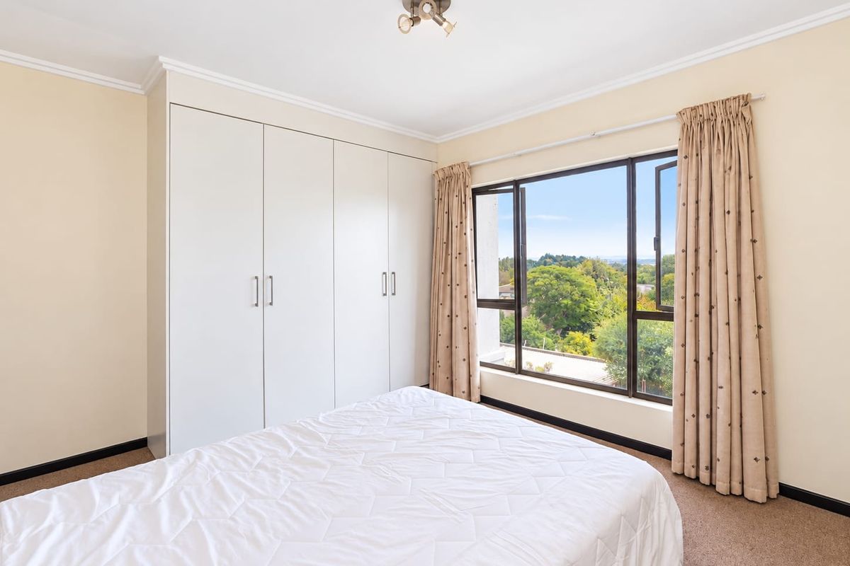A bright bedroom featuring built-in cupboards, carpeted flooring, and a large window offering pleasant outdoor views.