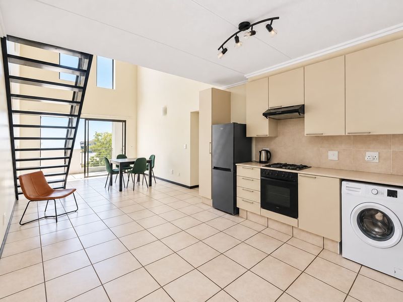 Spacious open-plan kitchen and living area featuring tiled floors, built-in cabinetry, modern appliances, and a striking metal staircase leading to an upper level.