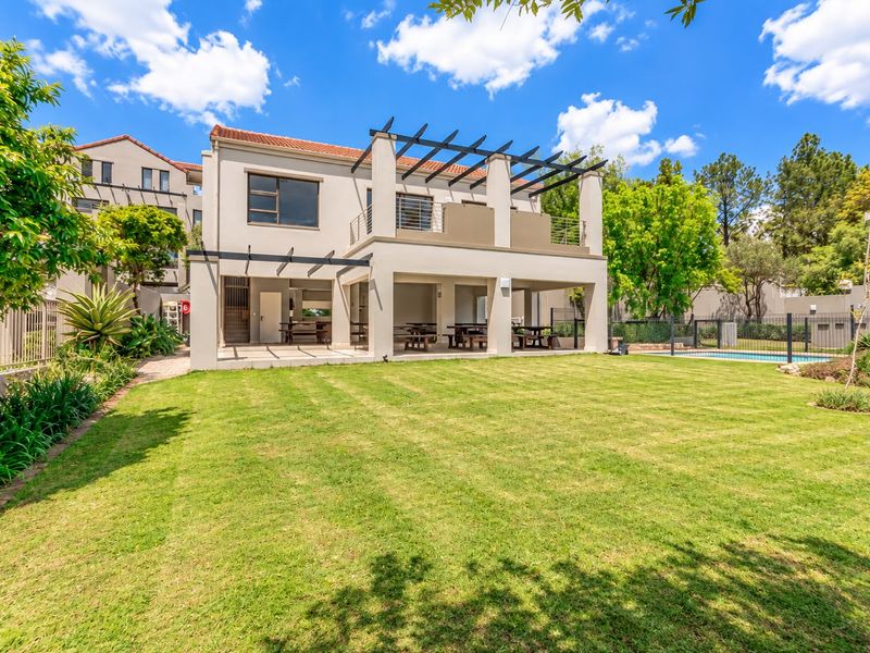 Rear view of the apartment building featuring a spacious lawn, covered patio area, upper balcony with pergola, and a swimming pool.