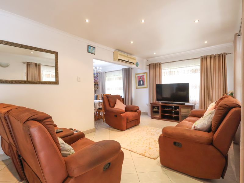 A well-maintained living room featuring tiled flooring, recessed downlighting, and a wall-mounted split-system air conditioner, with an open flow to the adjacent dining area.