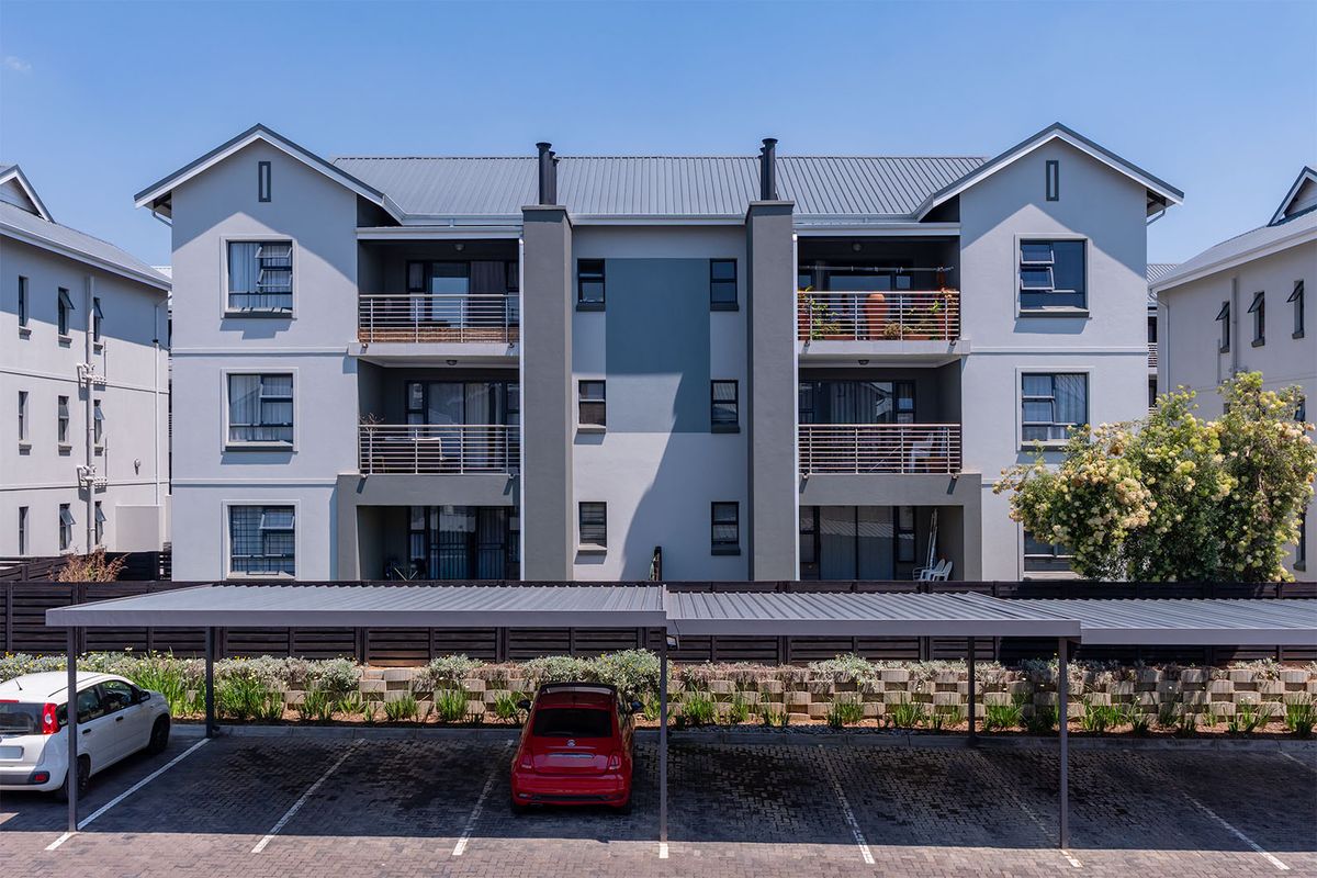 Rear view of a multi-story apartment complex featuring private balconies, a metal roof, and a covered carport parking area with paved bays.