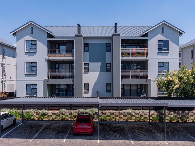 Rear view of a multi-story apartment complex featuring private balconies, a metal roof, and a covered carport parking area with paved bays.