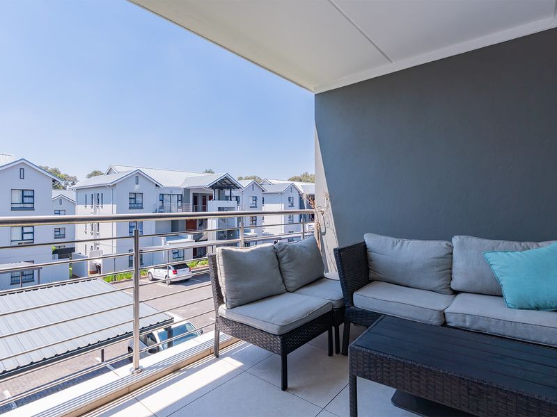 A covered balcony featuring tiled flooring and a modern stainless steel balustrade, offering an open view of the surrounding apartment complex.