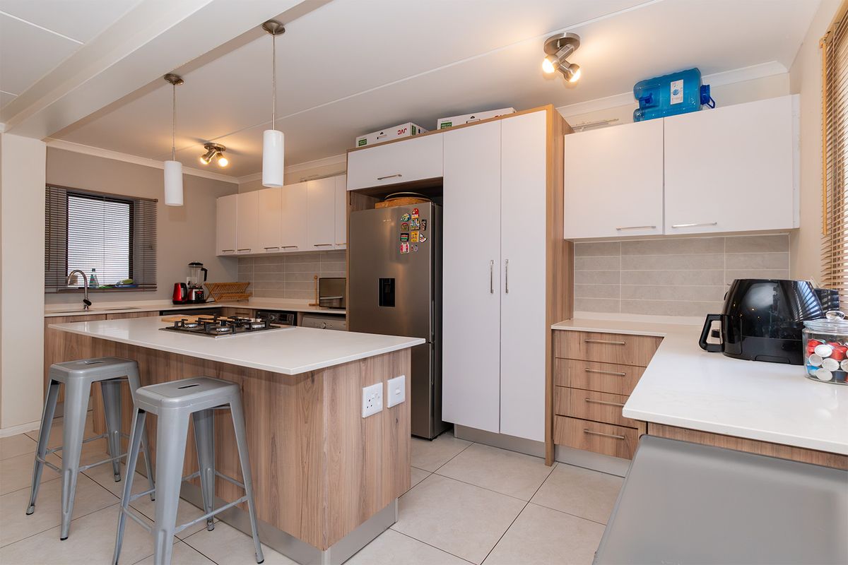 Modern kitchen featuring light wood-grain cabinetry, white stone countertops, a central island with a gas hob, and tiled flooring.