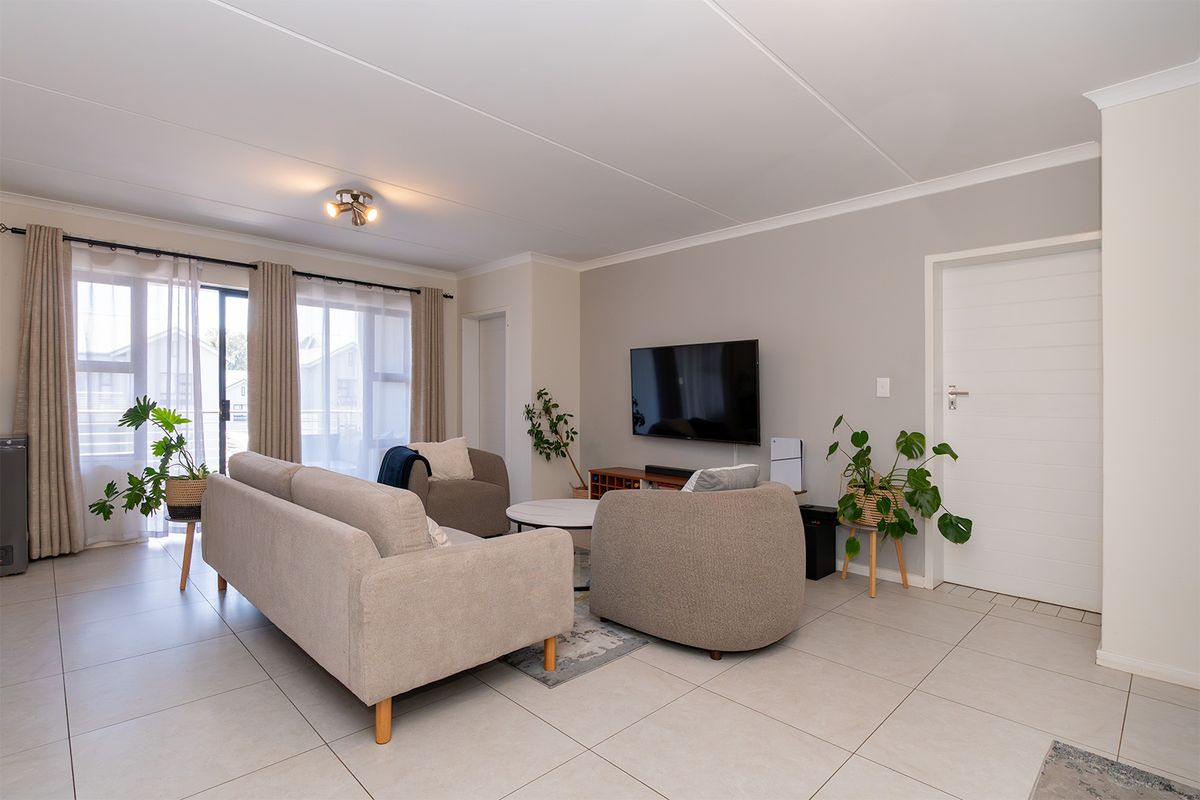 A bright and well-maintained living room featuring neutral tiled flooring, a sliding glass door providing natural light, and clean, modern finishes.