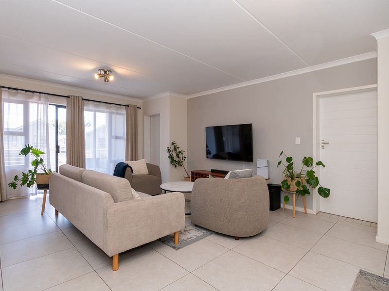 A bright and well-maintained living room featuring neutral tiled flooring, a sliding glass door providing natural light, and clean, modern finishes.