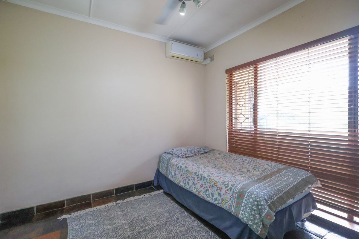 A functional bedroom featuring tiled flooring, a wall-mounted split-system air conditioner, and wooden venetian blinds for privacy.