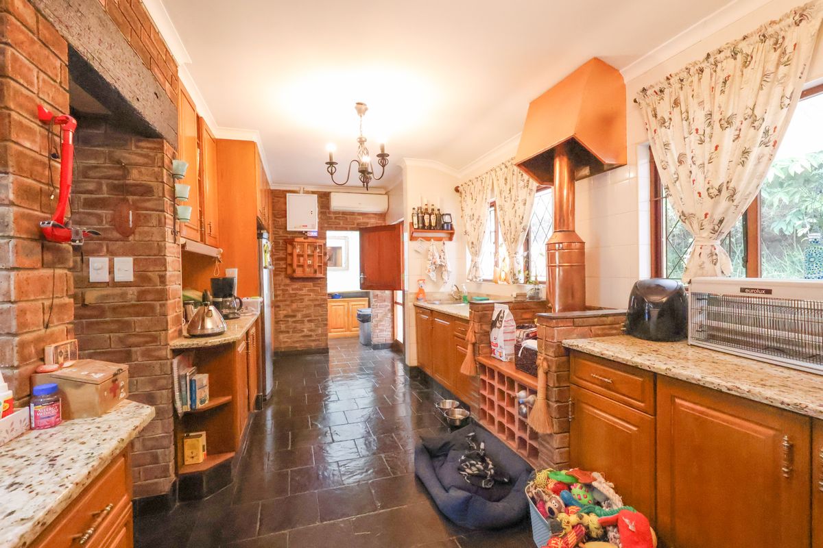A rustic-style kitchen featuring exposed brick walls, wooden cabinetry, granite countertops, and a distinctive copper extractor hood, complemented by dark slate tile flooring.