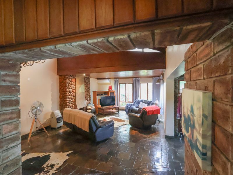 Spacious living room featuring rustic exposed brickwork, a stone fireplace, slate flooring, and exposed timber ceiling beams, creating a warm and character-filled atmosphere.