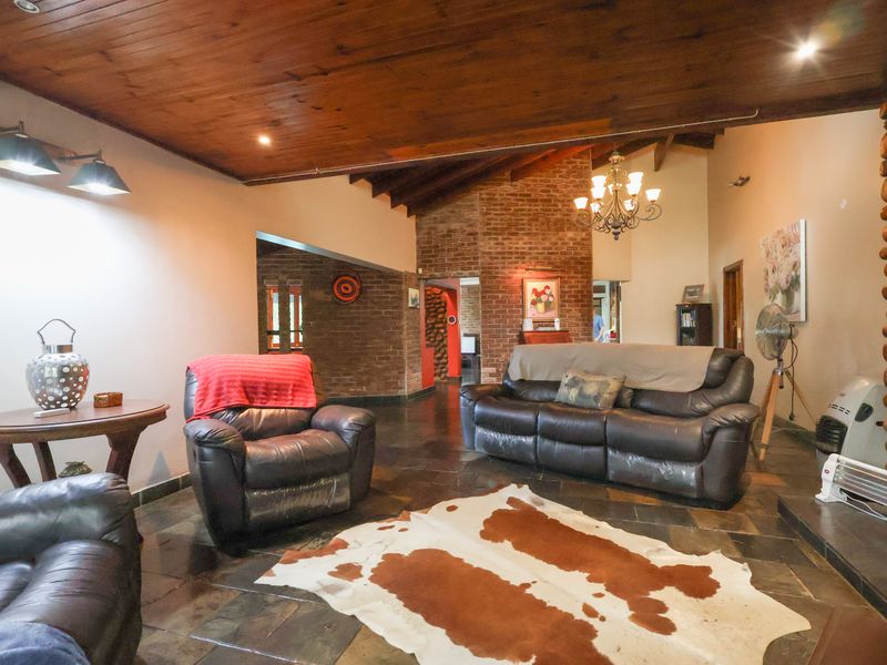 Spacious living room featuring a high exposed timber ceiling, stone tile flooring, and a prominent exposed brick feature wall.