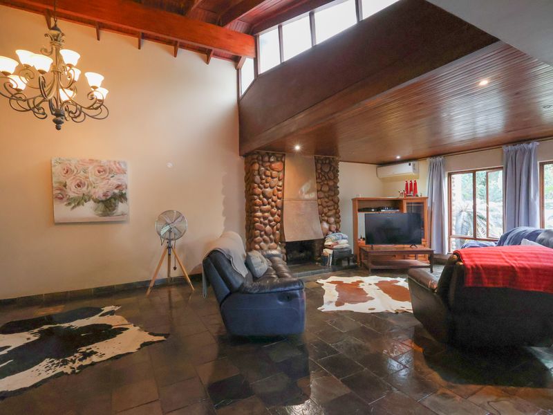 Spacious living room featuring high vaulted timber ceilings, a distinctive stone fireplace, and durable slate flooring with abundant natural light from clerestory windows.