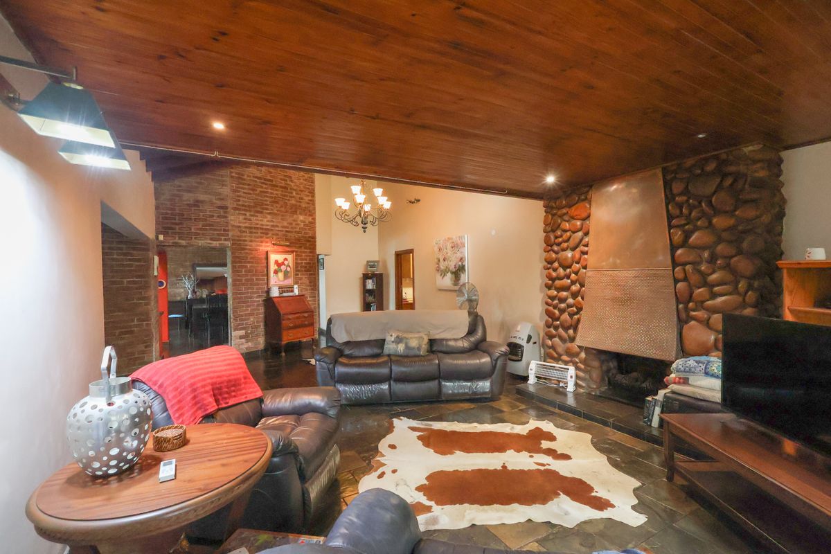 Spacious living room featuring a prominent stone fireplace, exposed brick accents, warm timber ceiling, and durable slate flooring.