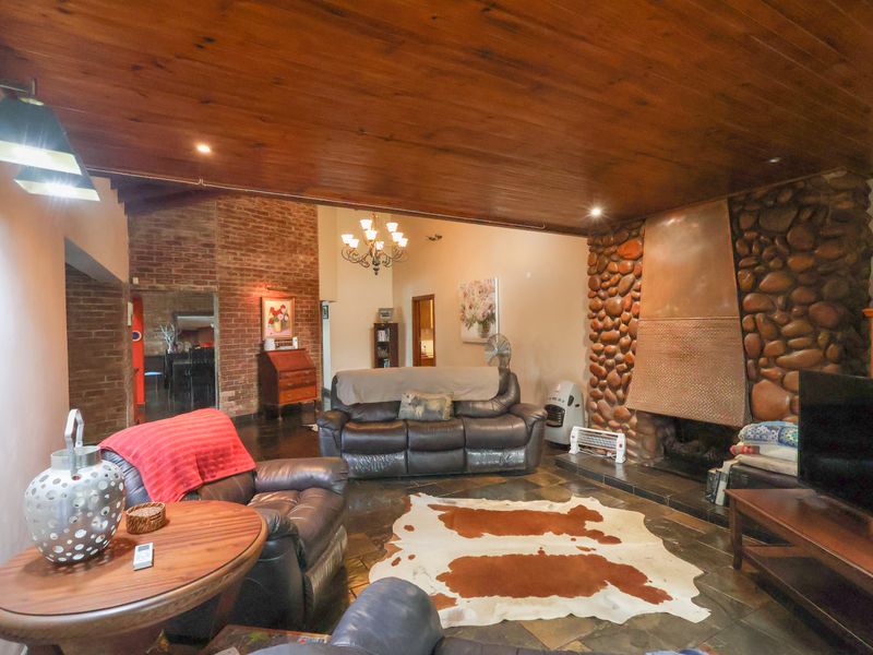 Spacious living room featuring a prominent stone fireplace, exposed brick accents, warm timber ceiling, and durable slate flooring.