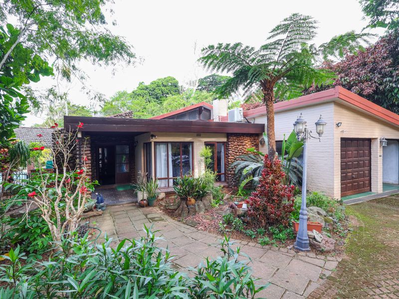 Front elevation of a house featuring stone and brick facade, paved walkway, and an integrated garage, set within a mature garden.