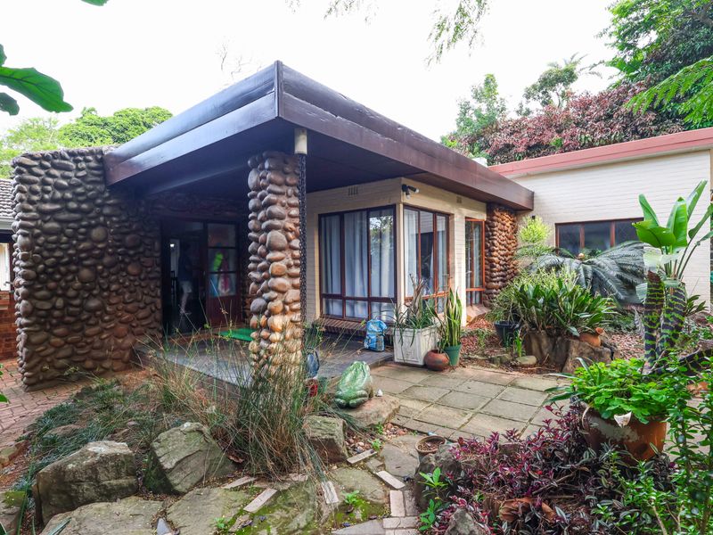 A covered patio area featuring unique stone cladding and a stone pillar, providing a sheltered outdoor space overlooking the garden.