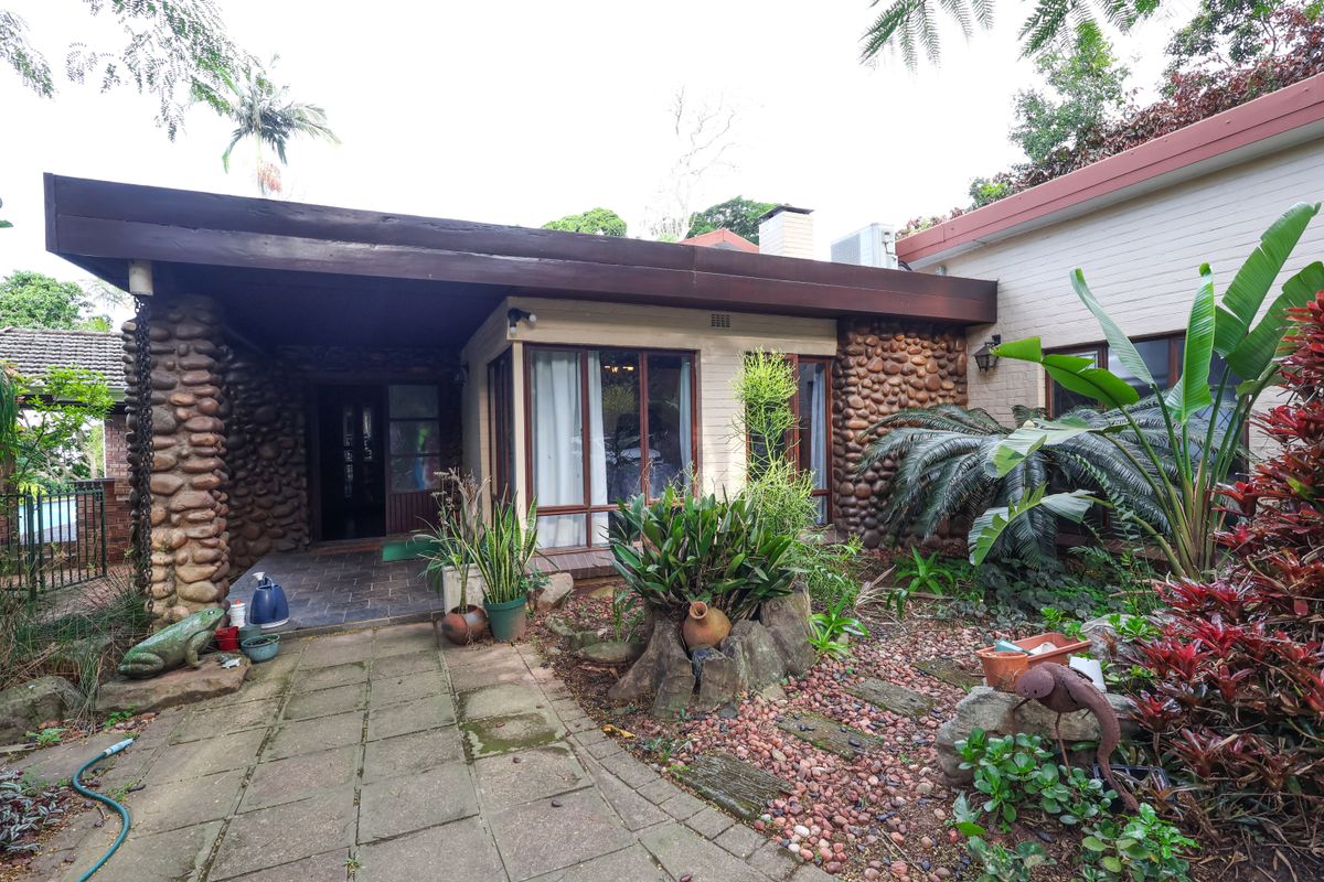 A rear exterior view featuring a covered patio, stone-clad walls, and a landscaped garden area with paved pathways.