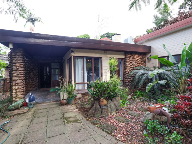 A rear exterior view featuring a covered patio, stone-clad walls, and a landscaped garden area with paved pathways.