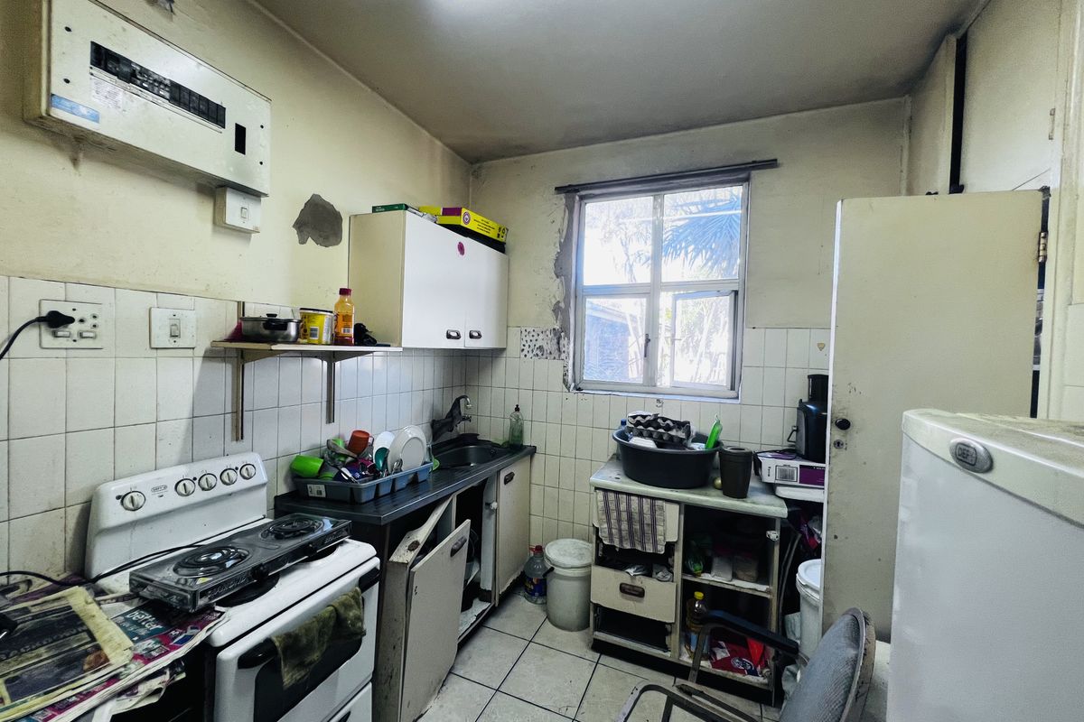 A dated kitchen featuring a built-in stove, tiled backsplash, and basic cabinetry, requiring significant renovation and repair to modernize the space.