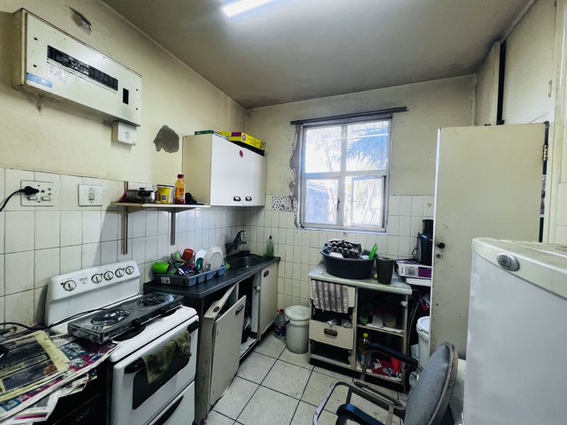 A dated kitchen featuring a built-in stove, tiled backsplash, and basic cabinetry, requiring significant renovation and repair to modernize the space.