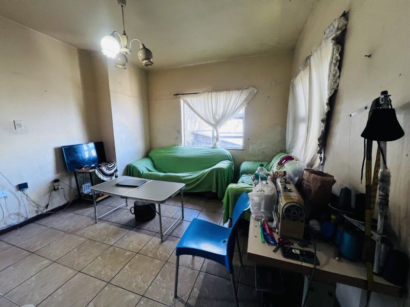 A living room space featuring tiled flooring and basic lighting, currently requiring significant cosmetic updates and wall repairs to improve its overall condition.