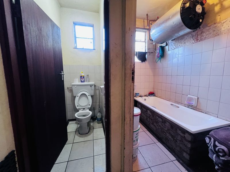 A dated bathroom featuring a separate toilet and bathtub area with exposed water heater and basic tiled finishes, requiring modernization and renovation.