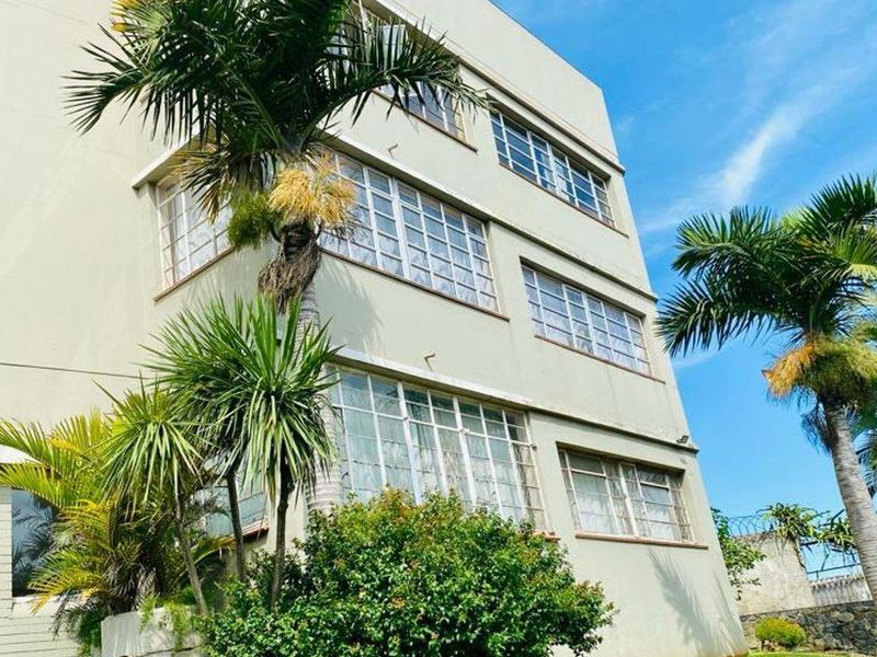 A low-angle view of a multi-story apartment building facade featuring classic multi-pane steel windows and a distinctive porthole window design.