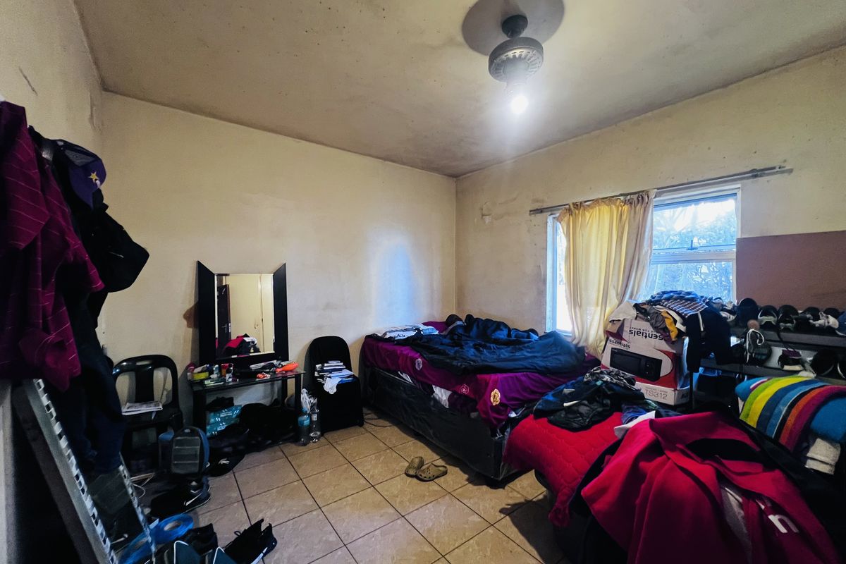 A bedroom featuring tiled flooring, a ceiling fan, and a window. The room requires significant cosmetic updates including painting and ceiling repairs.