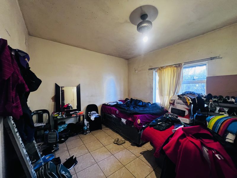 A bedroom featuring tiled flooring, a ceiling fan, and a window. The room requires significant cosmetic updates including painting and ceiling repairs.
