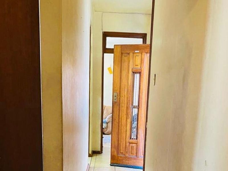 A narrow interior hallway featuring tiled flooring and wooden door frames, showing signs of wear and requiring cosmetic updates.