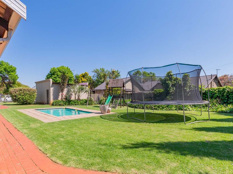 A well-maintained backyard featuring a swimming pool with paved surround, a brick patio area, and a spacious lawn.