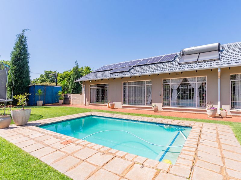 A well-maintained rear garden featuring a swimming pool, paved surround, and a house exterior equipped with solar panels and a solar water heating system.