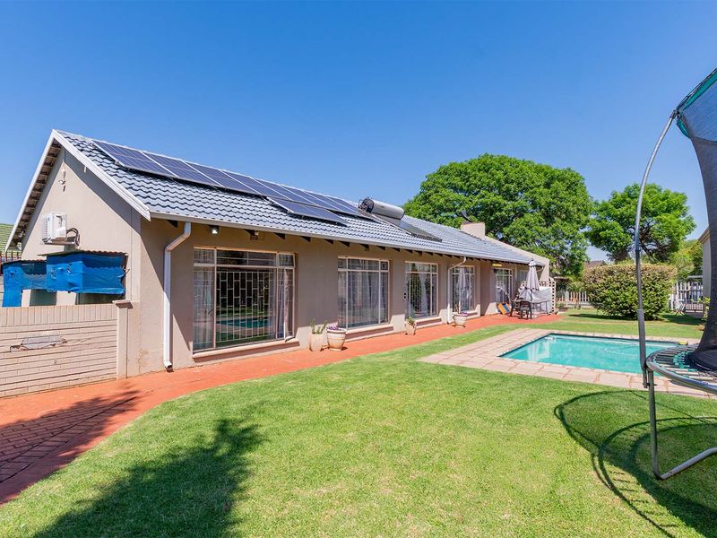 Rear exterior view of the house featuring a swimming pool, paved patio area, and roof-mounted solar panels and water heating system.