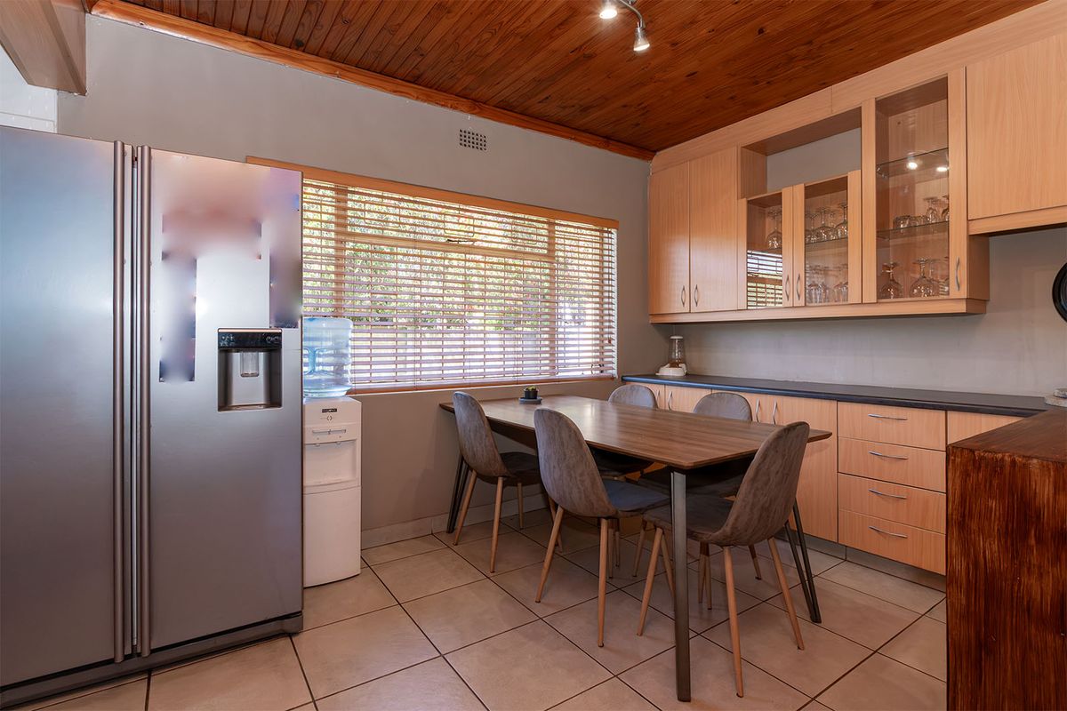 A functional kitchen area featuring light wood cabinetry, glass-fronted display units, tiled flooring, and a warm timber-paneled ceiling.