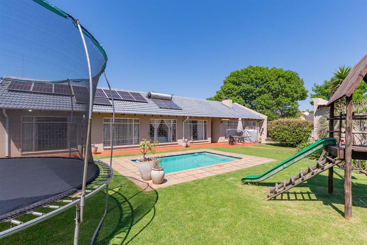 Rear exterior view of the house featuring a swimming pool, paved patio area, solar panels, and a well-maintained garden.