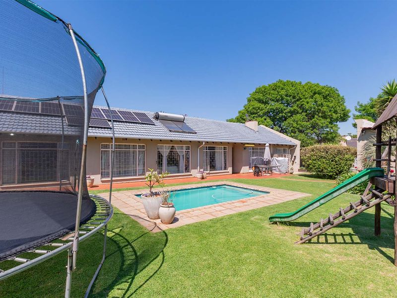 Rear exterior view of the house featuring a swimming pool, paved patio area, solar panels, and a well-maintained garden.