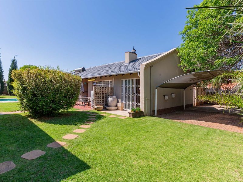 Rear view of the house featuring a well-maintained garden, paved driveway, carport, and a tiled roof with a solar water heating system.