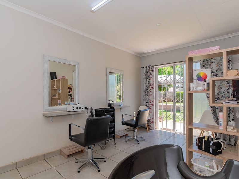 A functional utility space currently utilized as a salon, featuring tiled flooring, wall-mounted mirrors, and direct access to the rear garden via a sliding door.