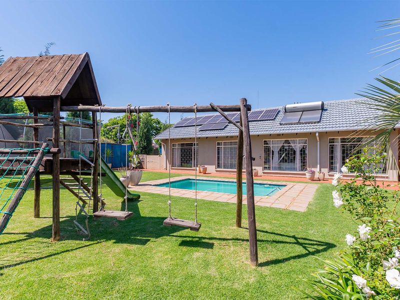 Rear exterior view featuring a swimming pool, landscaped garden, and a house equipped with solar panels and a solar water heating system.