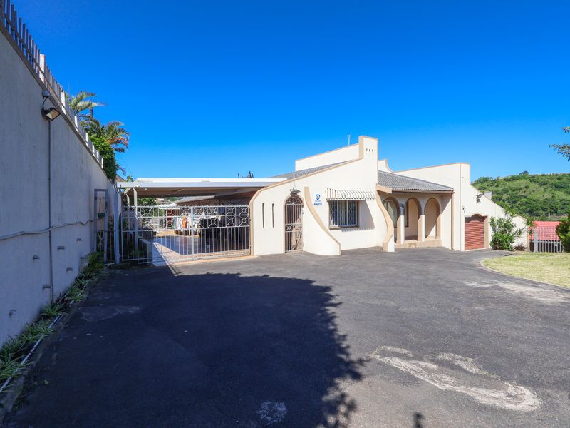 Front exterior view of the house featuring an asphalt driveway, a covered carport, and a secure perimeter wall.