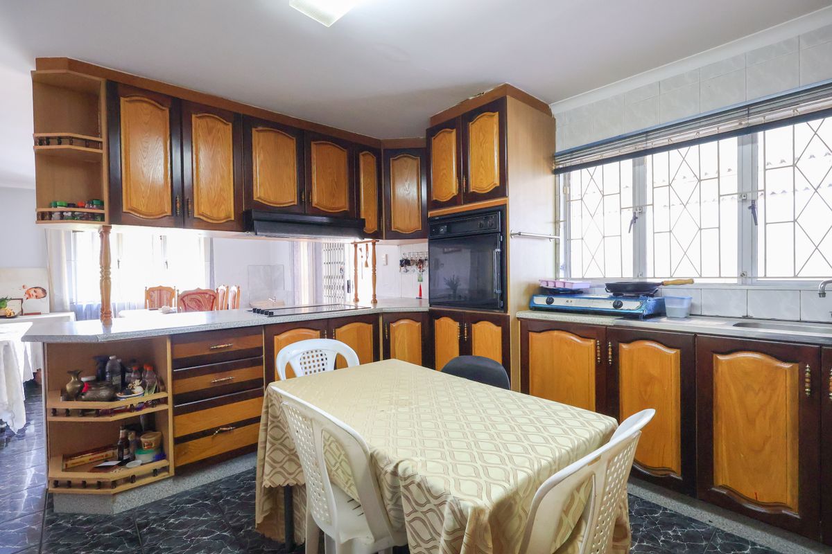 A functional kitchen featuring traditional wood-toned cabinetry, built-in oven, extractor fan, and tiled backsplash with security bars on the window.