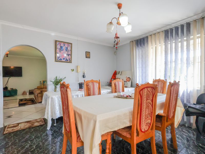 A dining room featuring tiled flooring, an arched entryway leading to an adjacent living space, and natural light through vertical blinds.