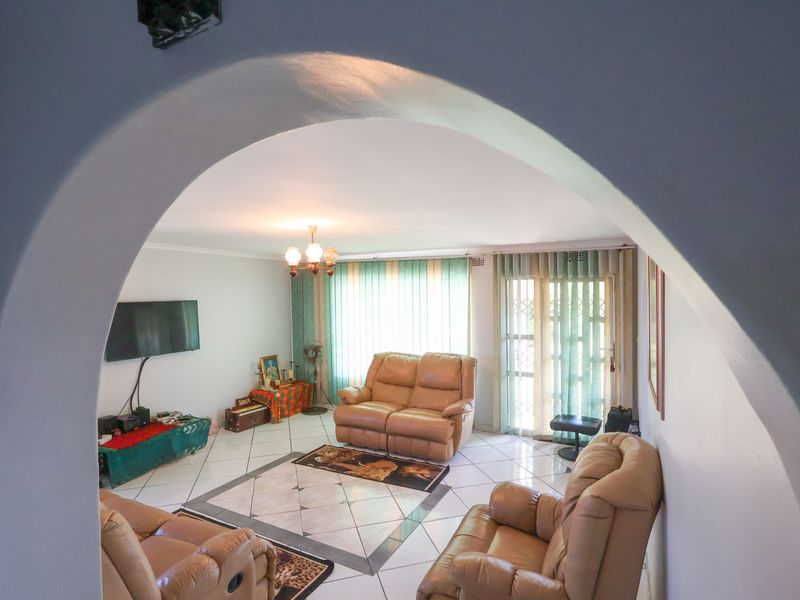 A living room featuring tiled flooring, an arched entryway, and a sliding glass door with security gate leading to the exterior.