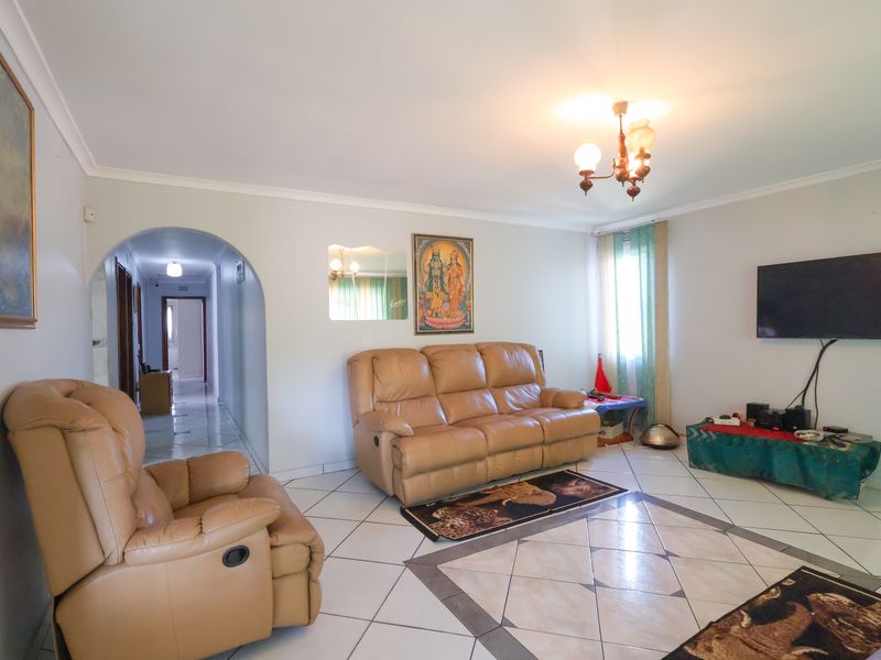 A spacious living room featuring tiled flooring, a decorative archway leading to the hallway, and coved ceiling details.