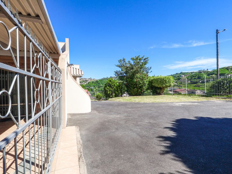 A view of the front exterior area featuring an asphalt driveway, secure metal fencing, and a covered patio entrance.