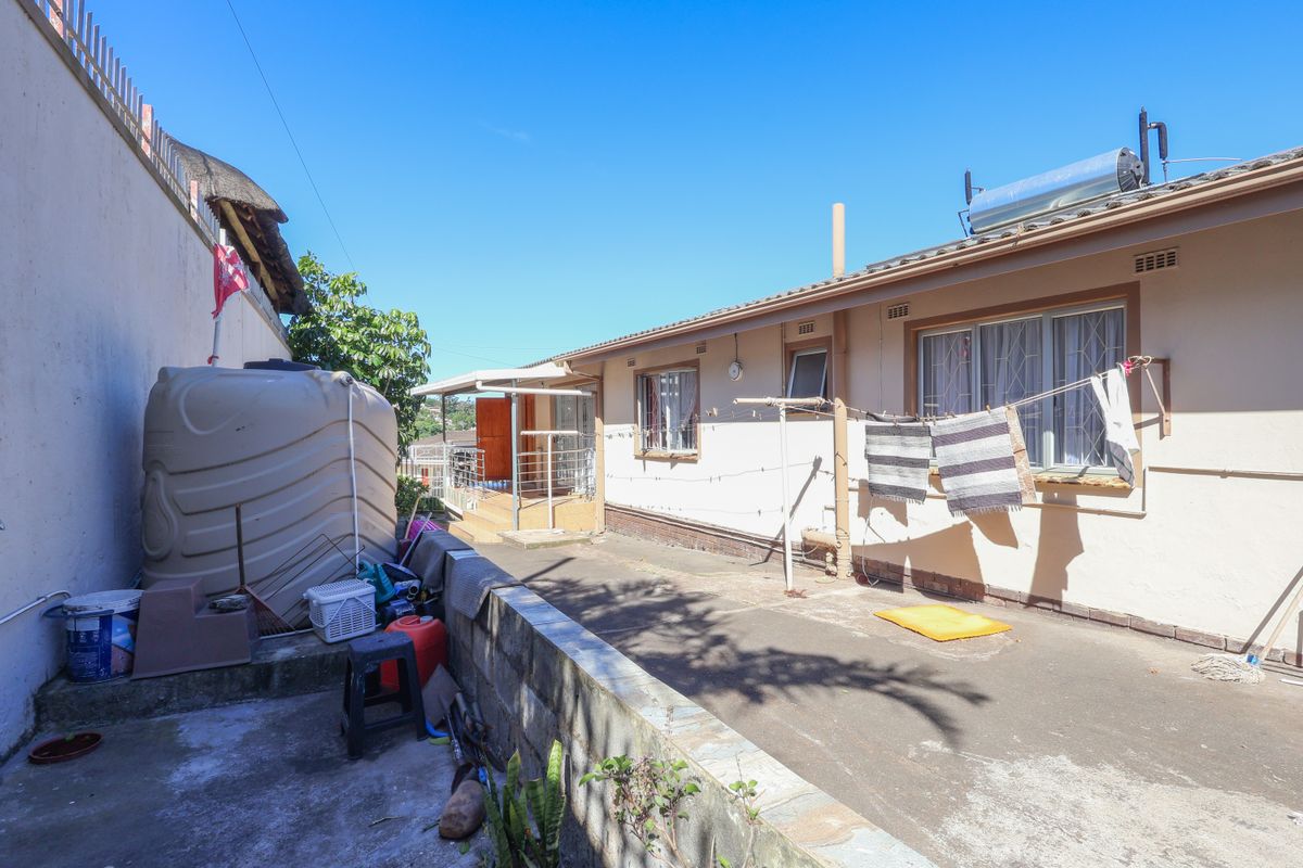 Rear exterior view of the property featuring a concrete paved area, water storage tank, and solar water heating system installed on the roof.