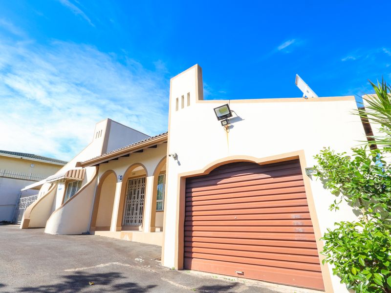 Front elevation of the property featuring a roller garage door, arched entrance with security gate, and paved driveway access.