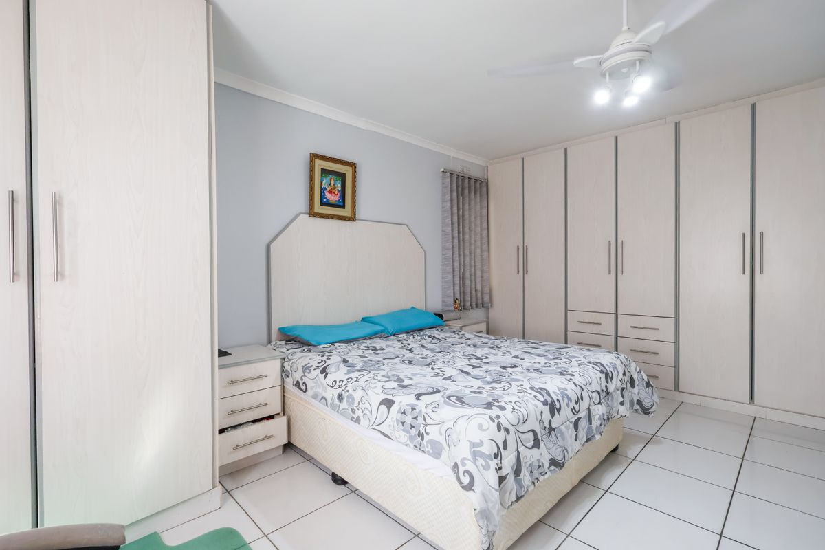 A well-maintained bedroom featuring extensive built-in cabinetry, a ceiling fan, and neutral tiled flooring, offering a clean and functional living space.