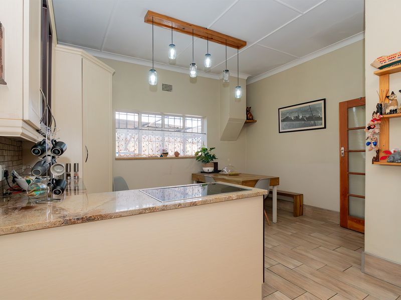 A well-maintained kitchen featuring granite countertops, a built-in hob, tiled flooring, and warm pendant lighting, creating a functional and inviting culinary space.
